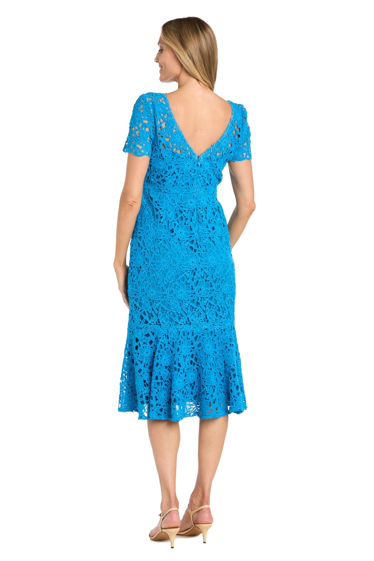 A woman faces away, wearing the R&M Richards 3498 midi lace wedding guest dress in bright blue with short sleeves and a V-back. She pairs the knee-length cocktail dress with beige heeled sandals.